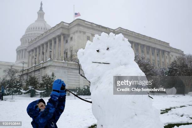 Boy gives a snow man stick arms in front of the U.S. Capitol March 21, 2018 in Washington, DC. An early spring storm brought several inches of snow...