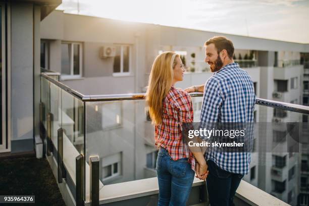 young happy couple holding hands and talking on a penthouse terrace, - couple balcony stock pictures, royalty-free photos & images