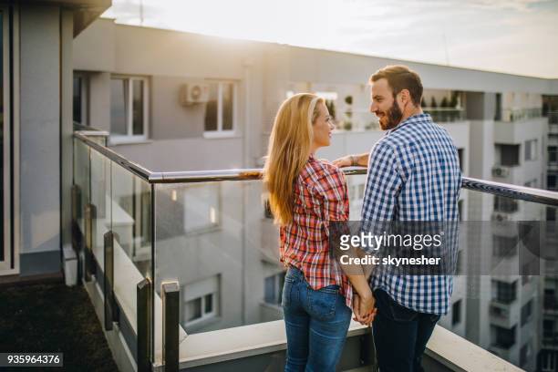 young happy couple holding hands and talking on a penthouse terrace, - apartamento de cobertura imagens e fotografias de stock