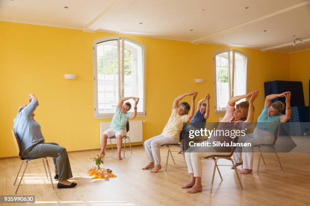 active senior women in yoga class exercisig on chairs, - chair stock pictures, royalty-free photos & images
