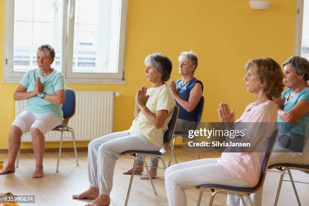 active senior women in yoga class exercisig on chairs - chair exercise stock pictures, royalty-free photos & images