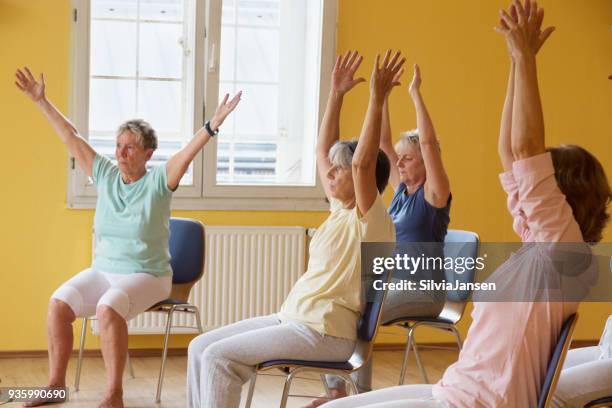 actieve senior vrouwen in yoga klasse exercisig op stoelen - chair exercise stockfoto's en -beelden