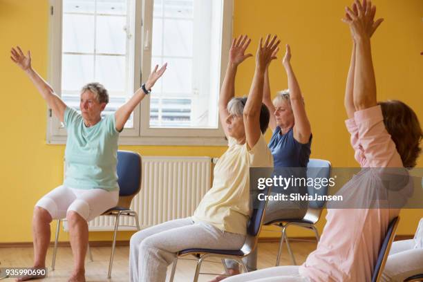 active senior women in yoga class exercisig on chairs - chair exercise stock pictures, royalty-free photos & images