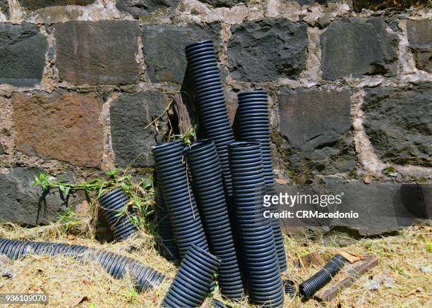pipes of power cables coming out of the ground on days of scorching sun next to a wall of stones. - crmacedonio stock-fotos und bilder