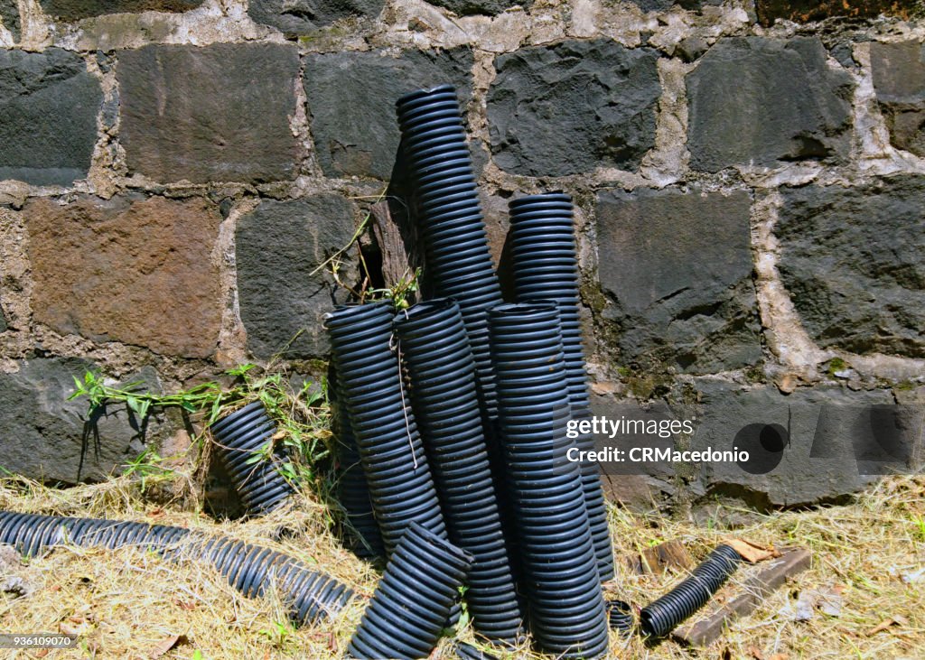 Pipes of power cables coming out of the ground on days of scorching sun next to a wall of stones.