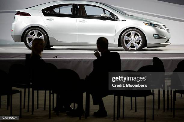 Attendees chat in front of a Chevy Volt on display at the 2009 LA Auto Show at the Los Angeles Convention Center in Los Angeles, California, U.S., on...