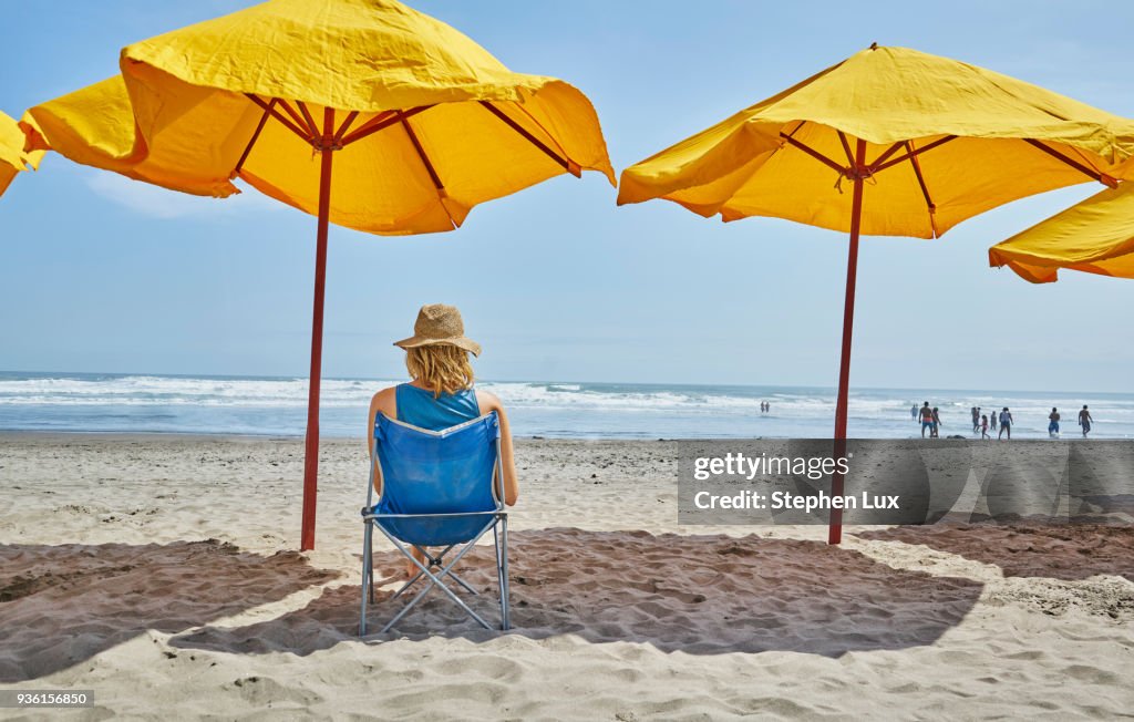 Rear view of female tourist sitting under beach umbrella, Camana, Arequipa, Peru