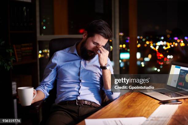 tired young businessman at office desk at night - koffeinmolekül stock-fotos und bilder