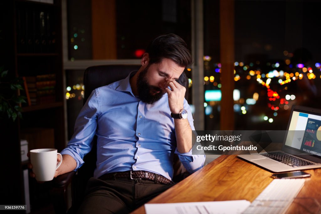 Tired young businessman at office desk at night