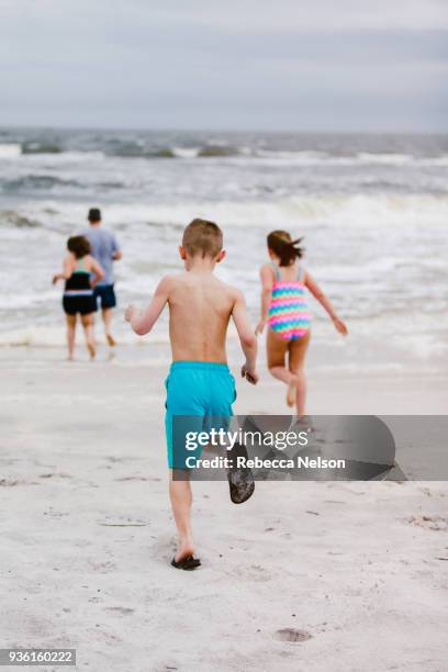 man and children running toward sea from beach, rear view, dauphin island, alabama, usa - alabama lifestyles stock pictures, royalty-free photos & images