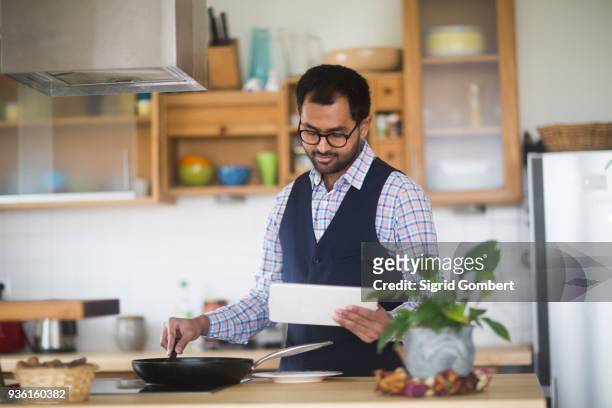 man cooking while using digital tablet at home - man glasses tablet in kitchen stock pictures, royalty-free photos & images