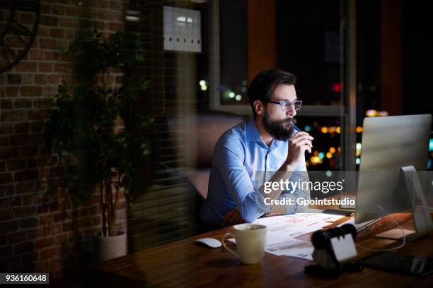 young businessman looking at computer on office desk at night - working overtime stock pictures, royalty-free photos & images