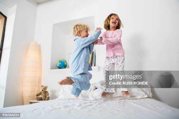 female and male twins jumping together on bed - children jumping bed stock-fotos und bilder