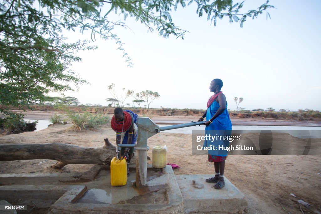 Women collecting clean water from borehole in desert. Samburu. Kenya.