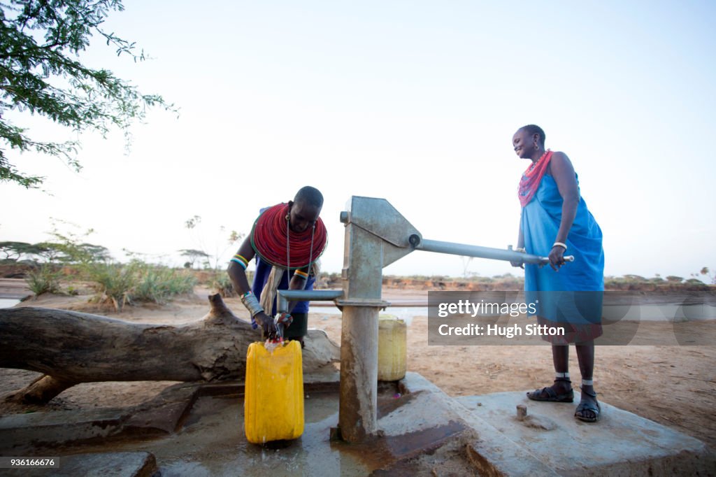 Women collecting clean water from borehole in desert. Samburu. Kenya.