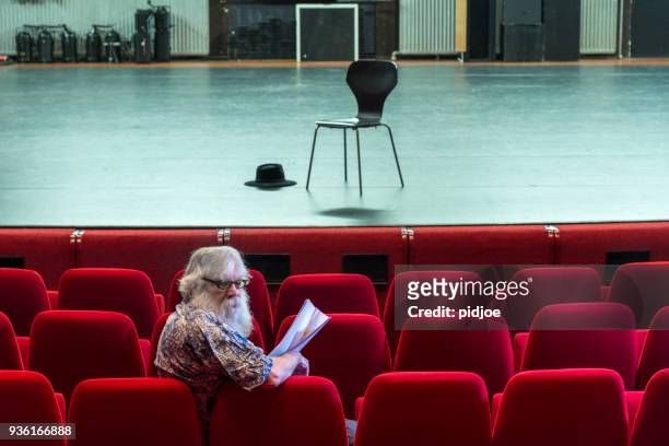 director working on a script in an empty theatre with red chairs and a empty stage - actor backstage stock pictures, royalty-free photos & images