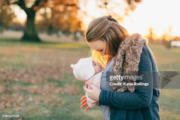 mother and baby daughter outdoors, mother carrying baby in baby sling - portabebés fotografías e imágenes de stock