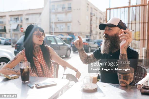 mature hipster couple chatting at sidewalk cafe, valencia, spain - couple in cafe man beard coffee stock-fotos und bilder