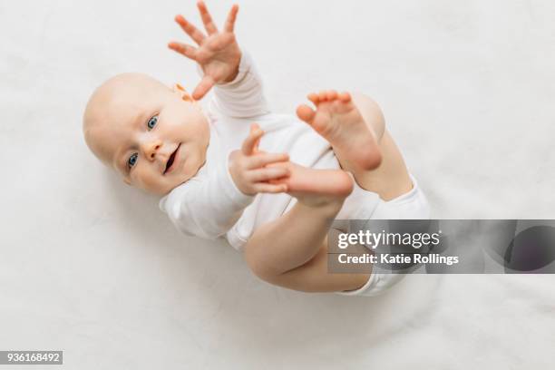 baby girl lying on back, arm and legs raised, looking at camera smiling - supino foto e immagini stock