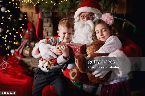 young girl and boy visiting santa, holding gifts - grotto stock pictures, royalty-free photos & images