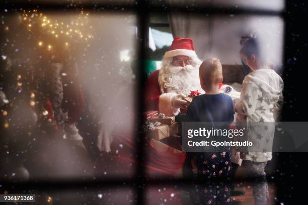 young girl and boy receiving gifts from santa, viewed through window - child christmas costume stock pictures, royalty-free photos & images