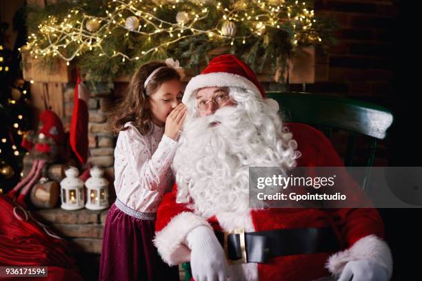 young girl visiting santa, whispering into santas ear - grotte stock-fotos und bilder