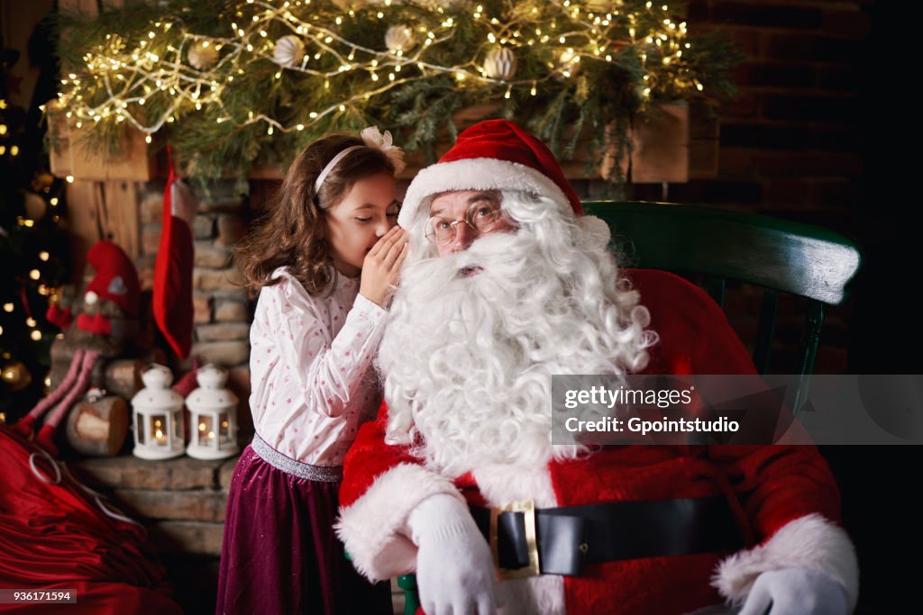 Young girl visiting Santa, whispering into Santas ear