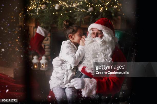 young girl sitting with santa, whispering into santas ear - grotto stock pictures, royalty-free photos & images