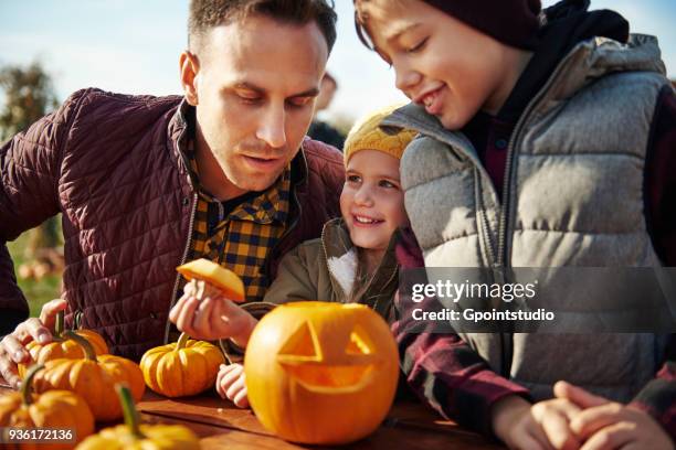 man with son and daughter looking at carved halloween pumpkin at pumpkin patch - girl face hat raincoat stock pictures, royalty-free photos & images