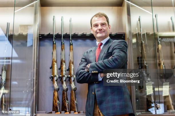 Christian Johann Springer, chief executive officer of Joh. Springer's Erben Handels GmbH, poses for a photograph against a rifle display case inside...