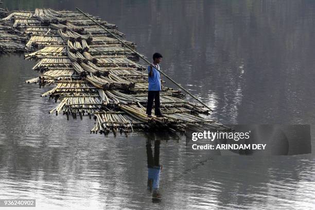 An Indian labourer pushes heaps of bamboo on a river to be sold at a floating market -- and set to be used in the construction industry -- in...