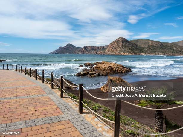 promenade and beach with volcanic rocks and sand with the waves in movement. - murcia - fotografias e filmes do acervo