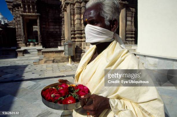 India, Gujarat, Palitana, Jain pilgrim with offering of flowers at Shatrunjaya or Place of Victory wearing white robe and scarf over mouth to avoid...