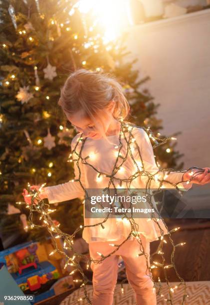 little girl (4-5) wrapped with christmas lights in living room - tetra images stock-fotos und bilder