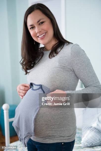 pregnant woman holding infant bodysuit in bedroom - baby clothing stock pictures, royalty-free photos & images