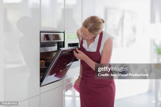 woman using oven in kitchen - horno cocina fotografías e imágenes de stock