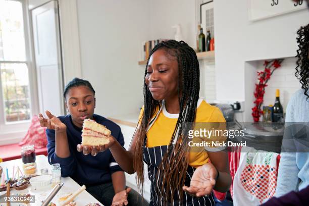two teenage girls (12-13, 14-15) eating cake in kitchen - david swallow stock pictures, royalty-free photos & images