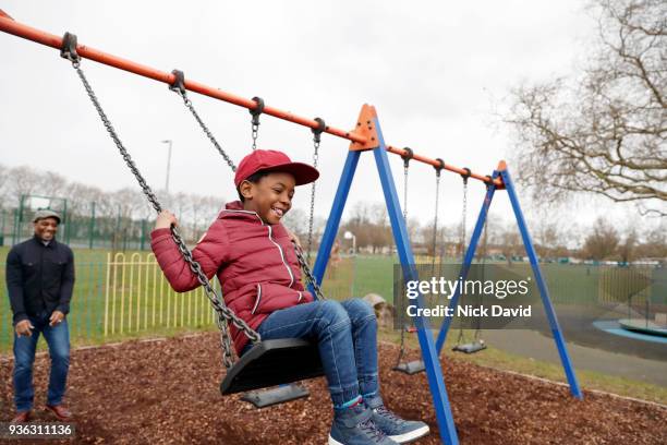 father pushing son (4-5) on swing in park - chain swing stock pictures, royalty-free photos & images