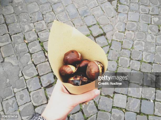 womans hand holding roasted chestnuts wrapped in paper - maroni stock-fotos und bilder