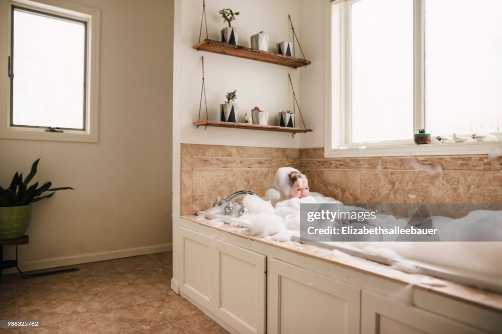 Boy sitting in a bubble bath laughing