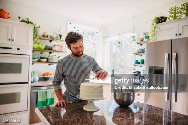 man standing in the kitchen decorating a cake - een taart bakken stockfoto's en -beelden