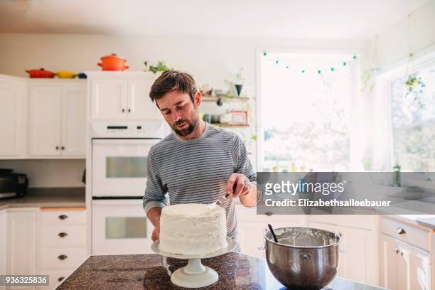 man standing in the kitchen decorating a cake - making a cake stock pictures, royalty-free photos & images
