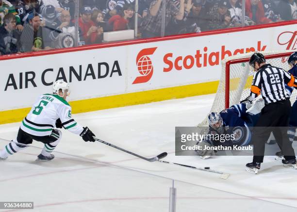 Goaltender Connor Hellebuyck of the Winnipeg Jets and Julius Honka of the Dallas Stars reach for the loose puck during second period action at the...
