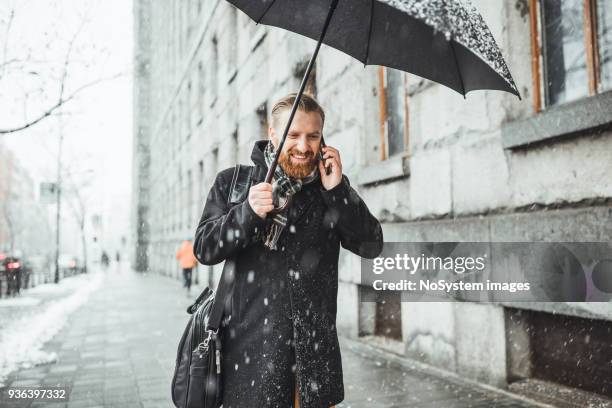 ginger businessman walking in the snow, under the umbrella, using smart phone. - corporate environment stock pictures, royalty-free photos & images