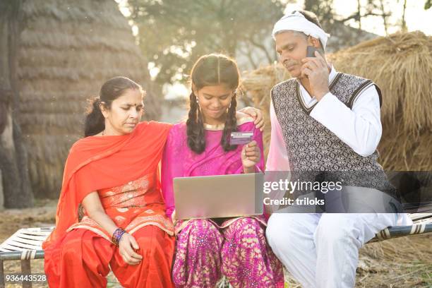 indische familie mit laptop und kreditkarte auf dorf bett - rural banking stock-fotos und bilder