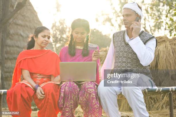 indische familie mit laptop und kreditkarte auf dorf bett - rural banking stock-fotos und bilder