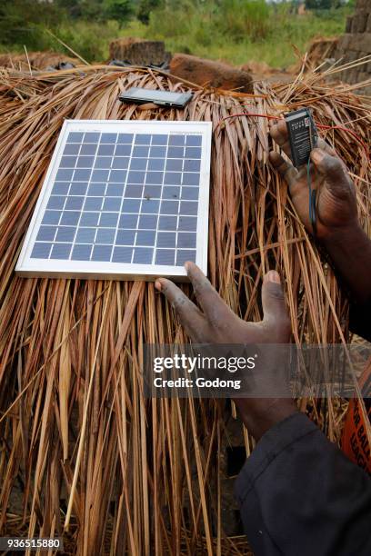 Brick factory worker using a solar panel to charge a cell phone battery. Uganda.