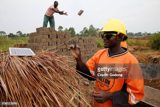 Brick factory worker using a solar panel to charge a cell phone battery. Uganda.