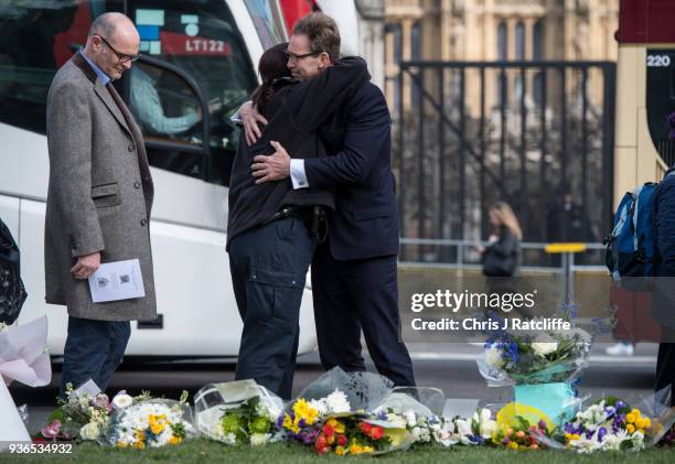 Tobias Ellwood embraces a female police officer next to floral tributes in Parliament Square on the first anniversary of the Westminster Bridge...