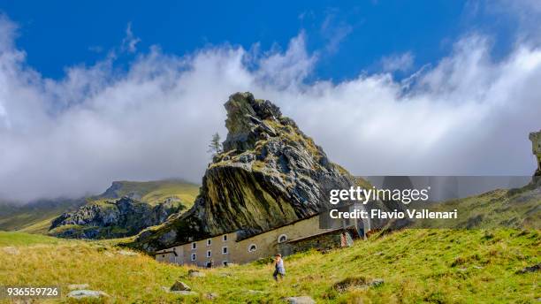 sanctuary of san besso, built with a side wall adjacent to the monolithic rock of mount fautenio. it is located in valle soana, a valley on the southern slope of the gran paradiso massif. gran paradiso national park, piedmont, italy - piedmont stock pictures, royalty-free photos & images